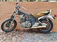 Full side view of the 1982 Yamaha XS400J Maxim motorcycle showing frame, engine, front and rear wheels, handlebars, and deteriorated seat with rust spots.