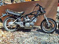 Side view of partial Yamaha motorcycle with frame, seat, engine, and wheels showing worn condition and missing parts.