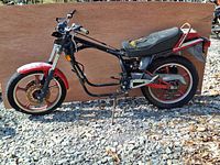 Side view of the partial motorcycle frame, showing black frame, red front and rear wheels, seat, and partial handlebar and front fork assembly.