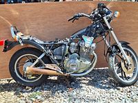 Side view of 1983 Yamaha XS400K Maxim motorcycle without seat and some parts; black frame, engine labeled Yamaha, visible rust on exhaust and metal parts