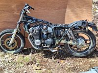 Side view of a 1984 Yamaha XJ750R Seca stripped frame with engine mounted. Visible inline four-cylinder engine, front wheel with disc brake, and rear wheel with drum brake setup. Frame is without body panels or seat, showing wear and surface rust.