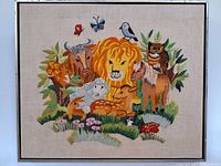 Full view of needlepoint artwork showing various animals and butterflies with floral and foliage background in a wooden frame.