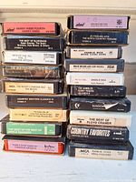 Stack of 18 assorted vintage 8-track tapes showing titles and artists including Harry Hibbs, Willie Nelson, Don Messer, Merle Haggard, Kenny Rogers, Charlie Rich, and The Beatles.
