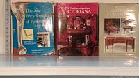 Front view of three hardcover books on antique furniture and Victoriana with visible wear on dust jackets.