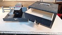 Slide projector with several components and carry case seen on table.