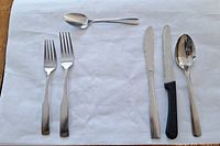 Six pieces of stainless steel cutlery displayed on white cloth including two forks, two knives, and two spoons.