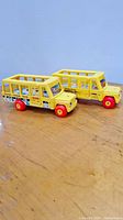 Two Fisher Price vintage yellow school buses displayed on wooden surface, showing one bus with wood flooring and driver and other fully plastic body