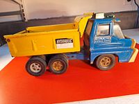 Side view of the blue and yellow pressed steel hydraulic dump truck toy with visible decals and wheels.