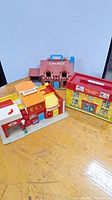 Front view of three vintage Fisher Price play buildings arranged side by side on a wooden surface.