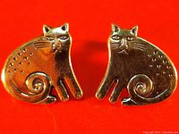 Front view of the cat-shaped earrings with spiral tail and dotted detailing on red background.