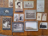 Top-down view of 14 various vintage black-and-white and sepia photographs spread out on a table, showing a range of portrait, group, and outdoor scenes from the 19th century.