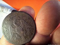 Close-up photo of the 1814 Lower Canada Half Penny Token held between thumb and forefinger, showing the eagle design and surrounding text.
