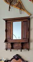 Side angled view of antique red oak wall hung mirrored shelf showing central mirror, side paneling, and wooden pegs.