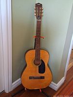 Full front view of the natural wood Canora acoustic guitar on a stand.