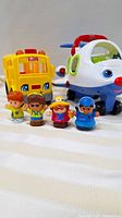 Photo showing yellow school bus, white airplane, and four Little People figures lined up in front