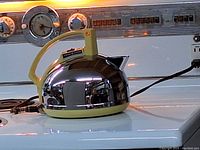 Side view of electric kettle on stove showing shiny chrome body and yellow handle.