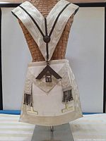 Frontal view of the Masonic apron and collar displayed on a mannequin torso, showing the apron with silver tassels and T-shaped metal accents, and the collar with large silver square and compasses pendant.