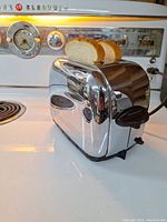 Side view of chrome toaster with two slices of bread placed on top showcasing size and use.