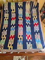 Full view of handstitched quilt laid out on a bed, showing patchwork pattern with alternating navy vertical strips and multicolored block patterns including reds, greens, and blues.