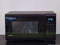 Photo of front view of Samsung microwave oven showing digital clock display 2:46, Samsung logo, and keypad panel.