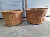 Two white oak bushel baskets side by side showing exterior with metal handles and bands.