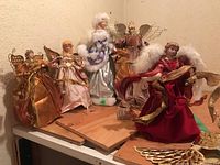 Five decorative treetop angels grouped on wooden base, various fabric dresses and wire wings visible.