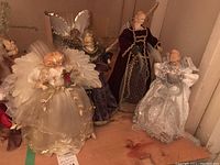 Six assorted angel tree toppers with varying wings and dresses, placed on wooden surface.