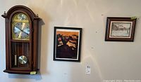 Wall clock hanging on wall next to two framed signed prints