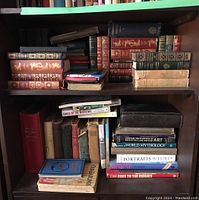 Bookshelves with a range of hardcover books mostly classic literature, mythology, and reference books, some showing significant wear and damage.
