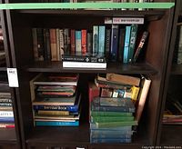Books on a wooden bookshelf, showing multiple rows with a mix of hardcover and softcover books, some stacked horizontally, titles visible include Becoming by Michelle Obama, and The Malta Exchange by Steve Berry