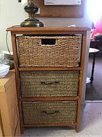 Front view of wood framed cabinet with three woven drawers; top drawer has woven pattern with cut-out handle, bottom two drawers have a different woven pattern with metal handles.