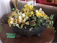 Front view showing embossed cast iron planter with detailed clawfoot legs and mixed yellow and white artificial flowers and green ivy