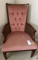 Front view of the chair showing pink tufted fabric backrest, dark stained wood frame, and wicker arm panels.