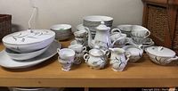 Overview of entire set including teapot, cups, plates, and platters arranged on wooden table with visible wear on gold trim and chip on some pieces