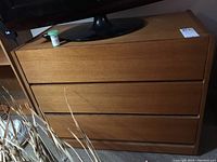 Three drawer wooden dresser with medium brown finish and flat drawer fronts photographed from two angles. Scratches and scuffs visible on surface.