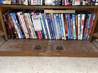 Photo showing a row of assorted DVD movies in plastic cases, approximately 36 in number, arranged on a wooden shelf.