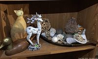 Shelf with a wooden cat figurine, wooden duck figurine, white deer figurine with metal antlers, natural twig balls, pine cone decor, and a Toby mug style candle holder.