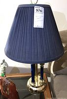 Photo of a single lamp off showing pleated blue shade and brass base with blue vertical accents.