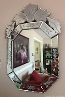 Full front view of the octagonal mirror hanging on the wall showing floral patterned etched glass and crack.