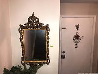 Full view of ornate brass mirror hung on wall with decorative top and bottom scrollwork