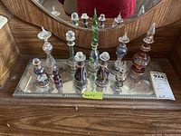 Full view of all 10 glass perfume bottles on the mirrored metal tray, showing variety in size and color, overall condition, and layout.