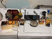 Wide image showing the entire set of vintage film equipment including camera, reels, film canisters, film viewer, tripod, and pamphlets arranged on a washer.