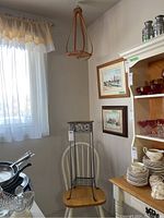Full view of hanging wooden plant stand suspended from ceiling above chair, next to framed pictures on wall.