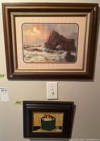Two framed prints on wall above light switch, seascape above and cat in basket below