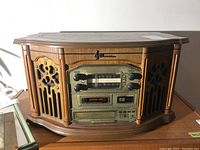 Front angled view of Emerson NR305TTC retro style stereo showing radio tuner dial, cassette player slot, decorative speaker grilles, and control knobs.