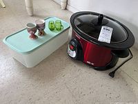 Rival slow cooker, white Tupperware container, two egg cups and green salt and pepper shakers arranged on floor
