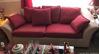 Front view of three-seat fabric sofa with beige base and red seat and back cushions along with throw pillows arranged on it.