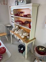 Table and hutch displayed with dishes and glassware, showing wood tabletop, painted legs, and hutch shelves with natural wood back panel.