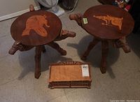 Photo of two Egyptian carved wood folding camel tables with inlaid tabletop designs and carved wood jewelry box on floor.