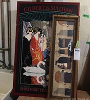 Two framed wall art pieces: a colorful Gilbert & Sullivan poster from the Stratford Festival, and a narrow framed cat folk art print.